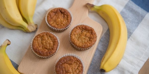 cutting board with banana muffins on it and bananas beside
