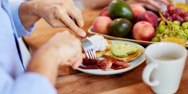 man eating off a plate of food with bacon toast avocado and fruit