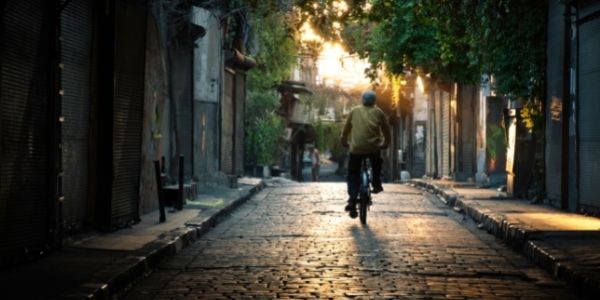 older person riding a bike down a cobble stone road