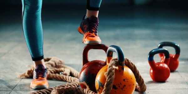 lady in running shoes with one shoe on a big kettlebell