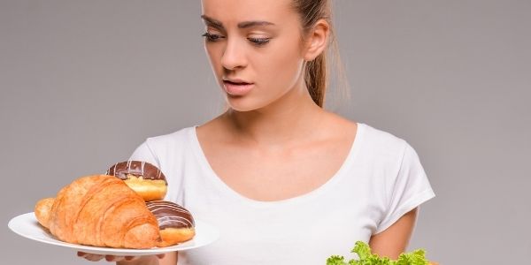 lady looking at a plate of pastries in one hand with a plate of lettuce on a plate in the other hand