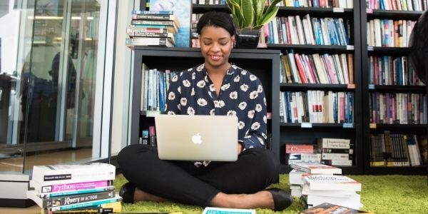 lady sitting on the floor with a laptop surrounded by books