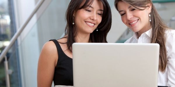 two women smiling at their laptop