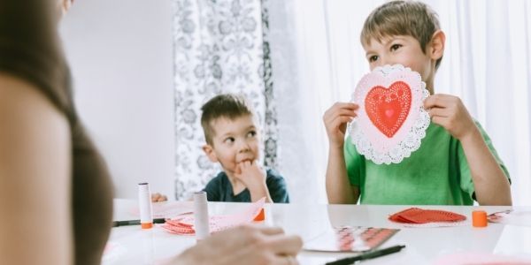 two kids sitting across from mom showing her valentines day card