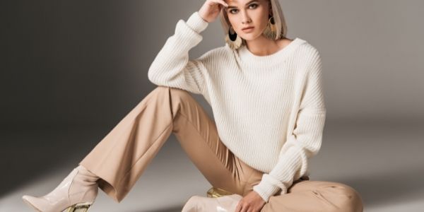 lady dressed in creamed color pants, cream heeled boots white knitted sweater and gold and black earrings