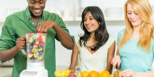 three people making smoothies with a blender