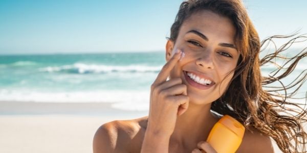 lady on a beach putting on sunscreen