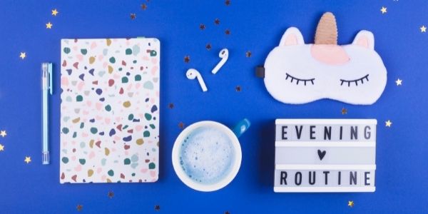 blue table with note book headphones eye mask tea sign that says evening routine