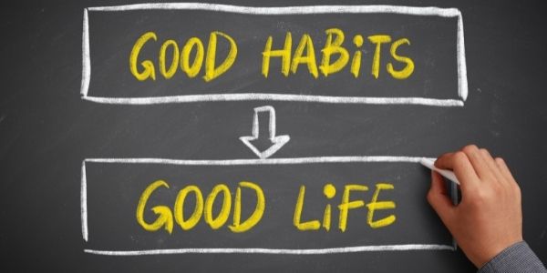 person writing on chalk board good habits arrow pointing to good life