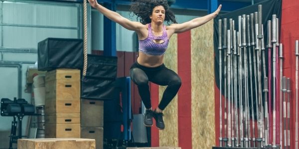 lady jumping with arms spread looks like a crossfit gym behind her