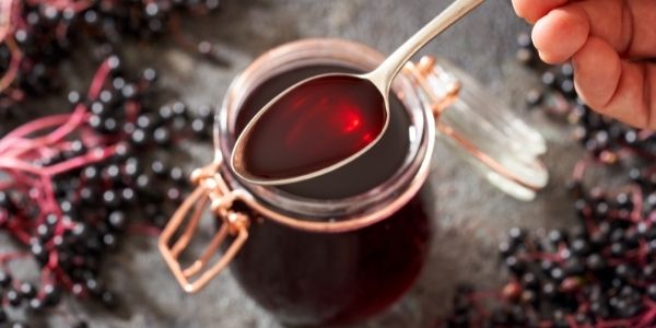 elderberry syrup in a cup with berries around it