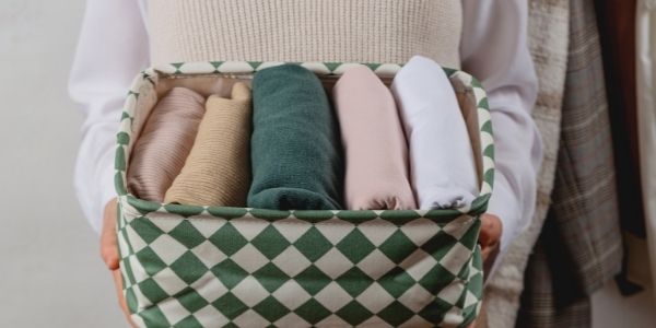 person holding a basket of 5 pieces of folded clothes