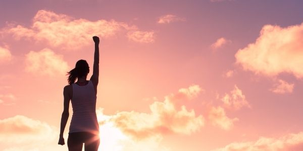lady standing in front of pink sunset with arm raised