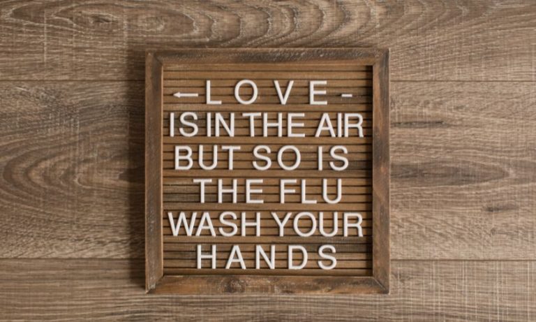 wooden letter board with white letters that say love is in the air but so is the flu wash your hands